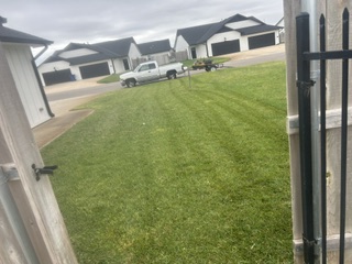 A freshly striped lawn with a work truck parked on the street beside a fence